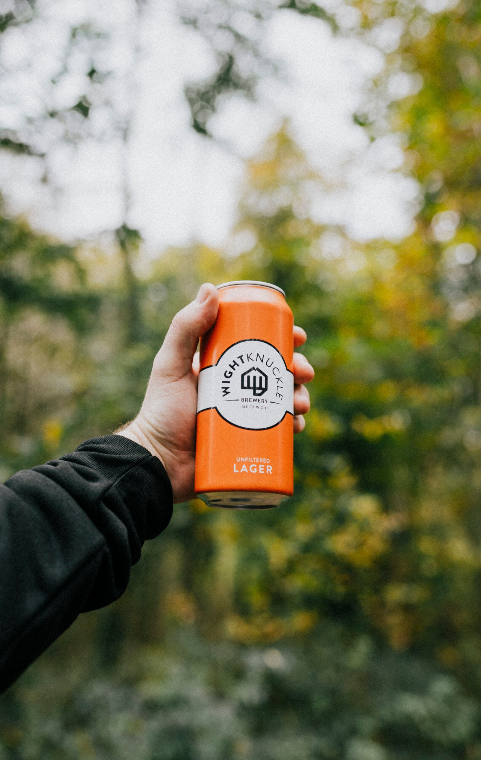 A can of Wight Knuckle Brewery unfiltered lager held up in Isle of Wight woodland