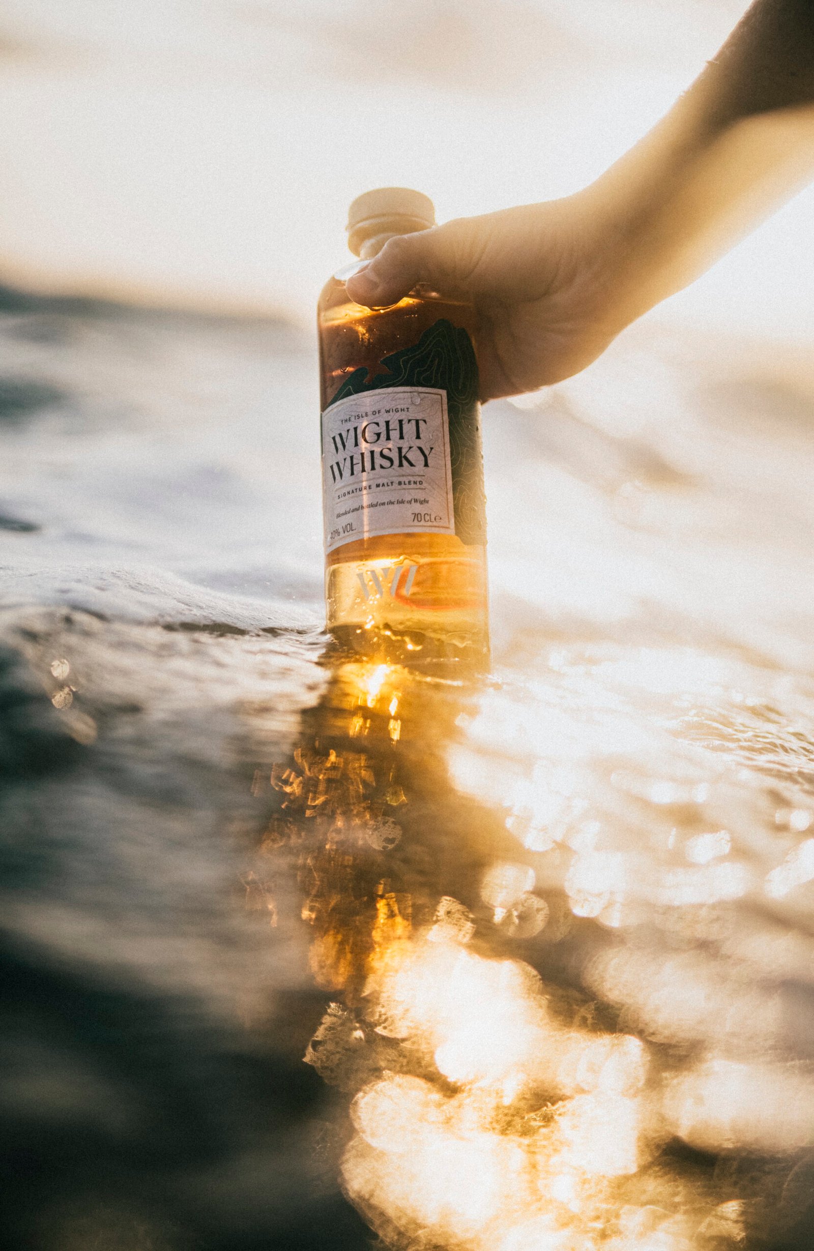 A bottle of Wight Whisky held above the sea at golden hour